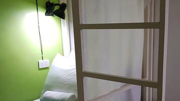 A bunk bed room with a green wall, a white bed, and a blue towel on the lower bunk.