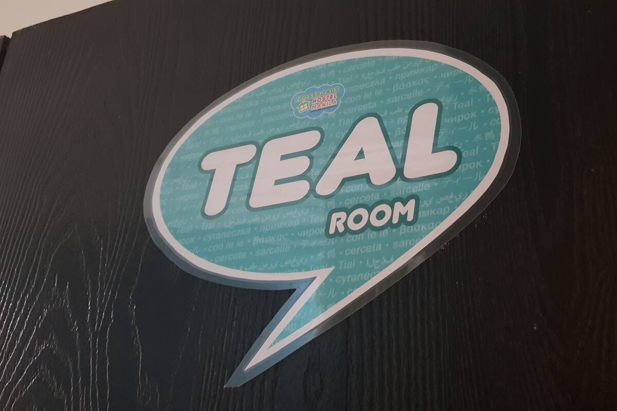 A sticker on a black surface with the text "TEAL ROOM" and a logo that reads "CRISSPROADS HOSTEL MANILA".