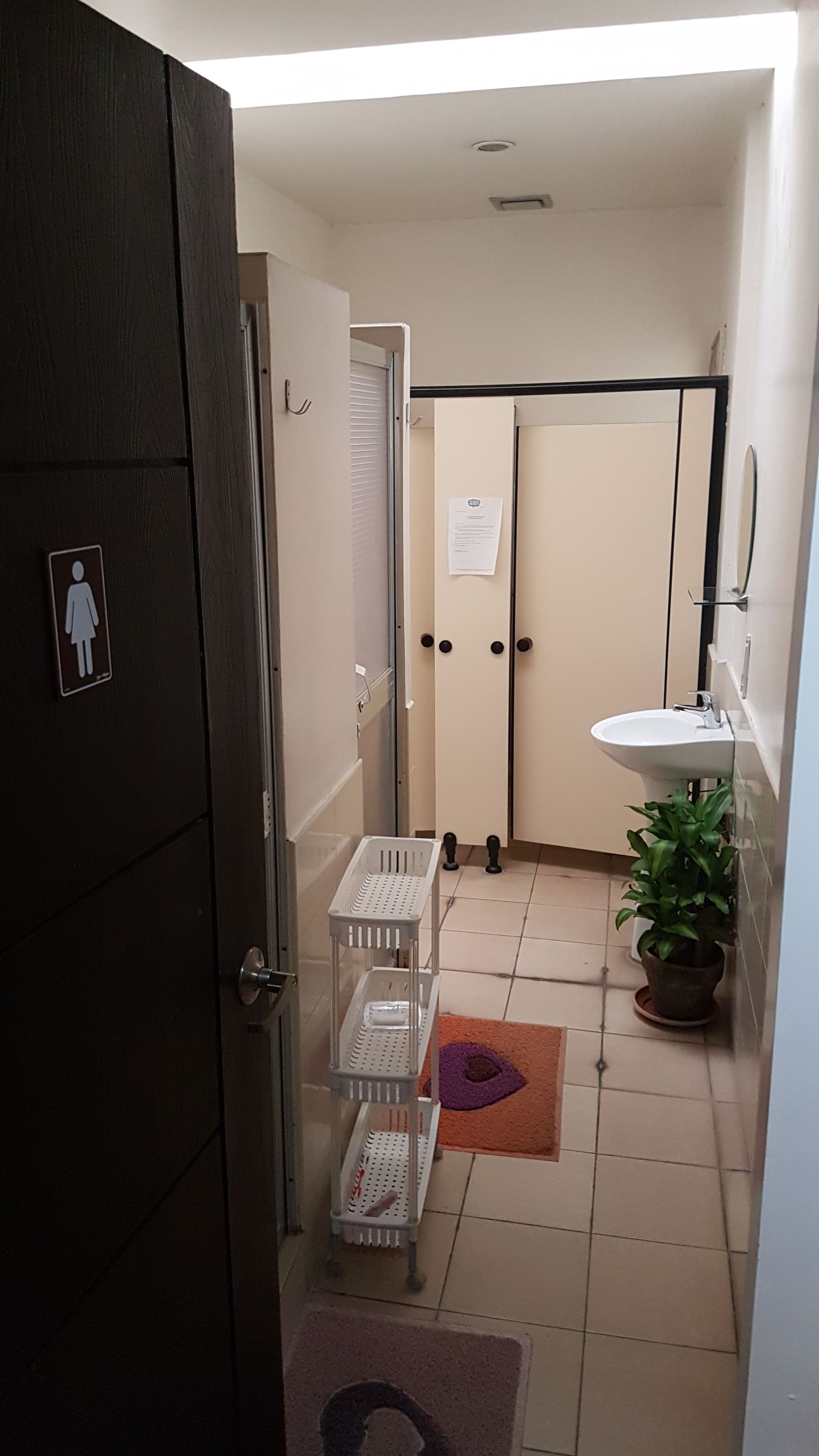 A narrow hallway with a door marked for female guests, a white sink, a potted plant, and a tiled floor.