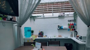 A compact kitchen with a dining table, chairs, a water dispenser, and a refrigerator. - Crossroads Hostel Manila (Mandaluyong)