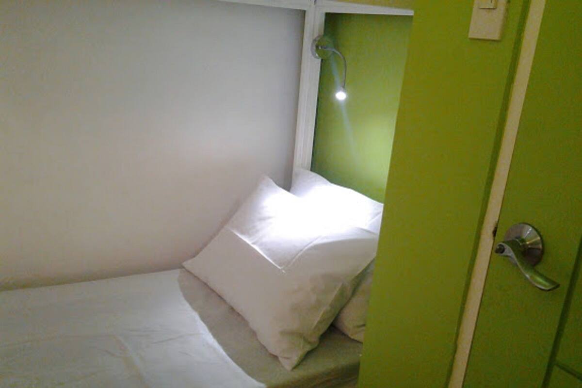 A single bed with white bedding in a room with green walls and a door.
