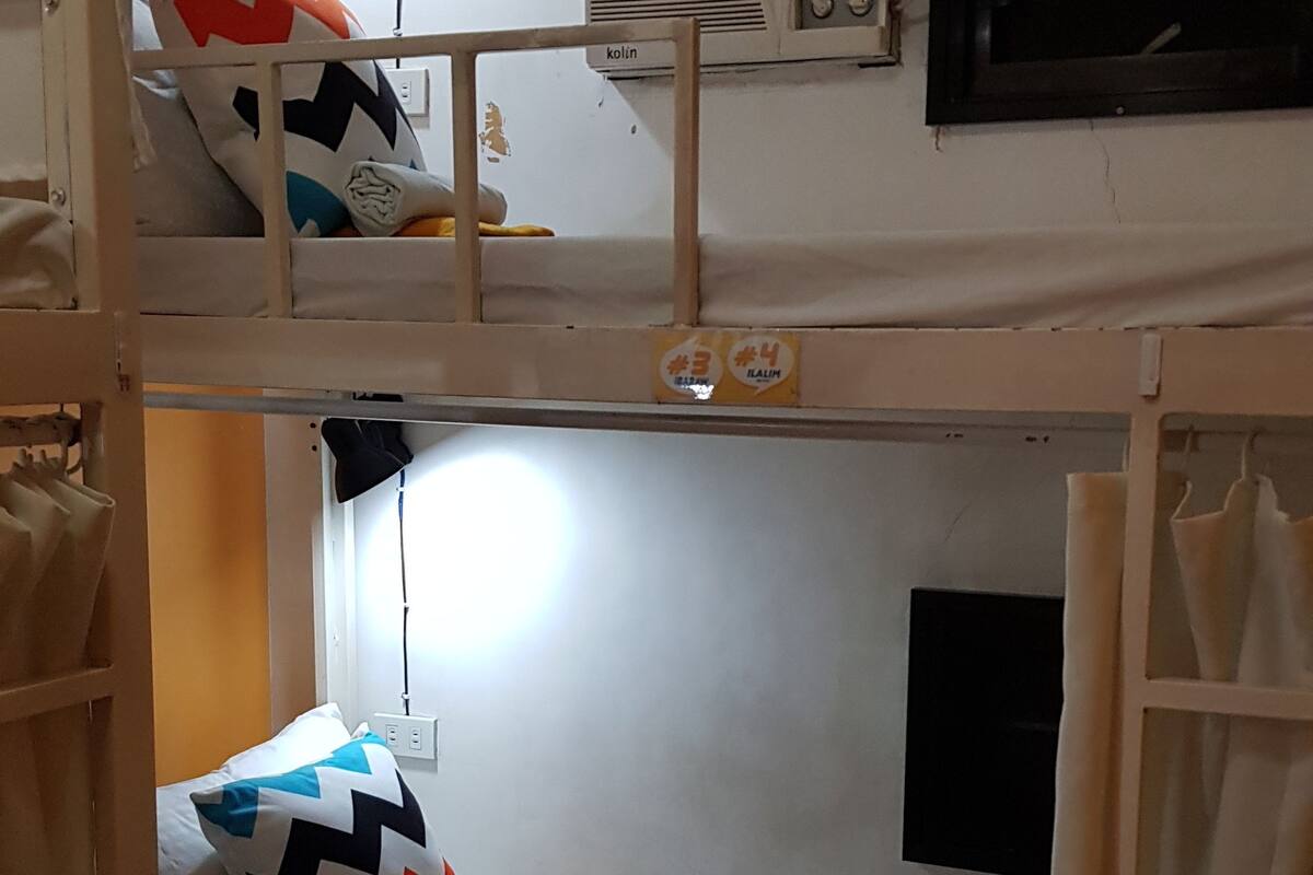 A bunk bed room with a ladder, a desk, a lamp, and an air conditioning unit.