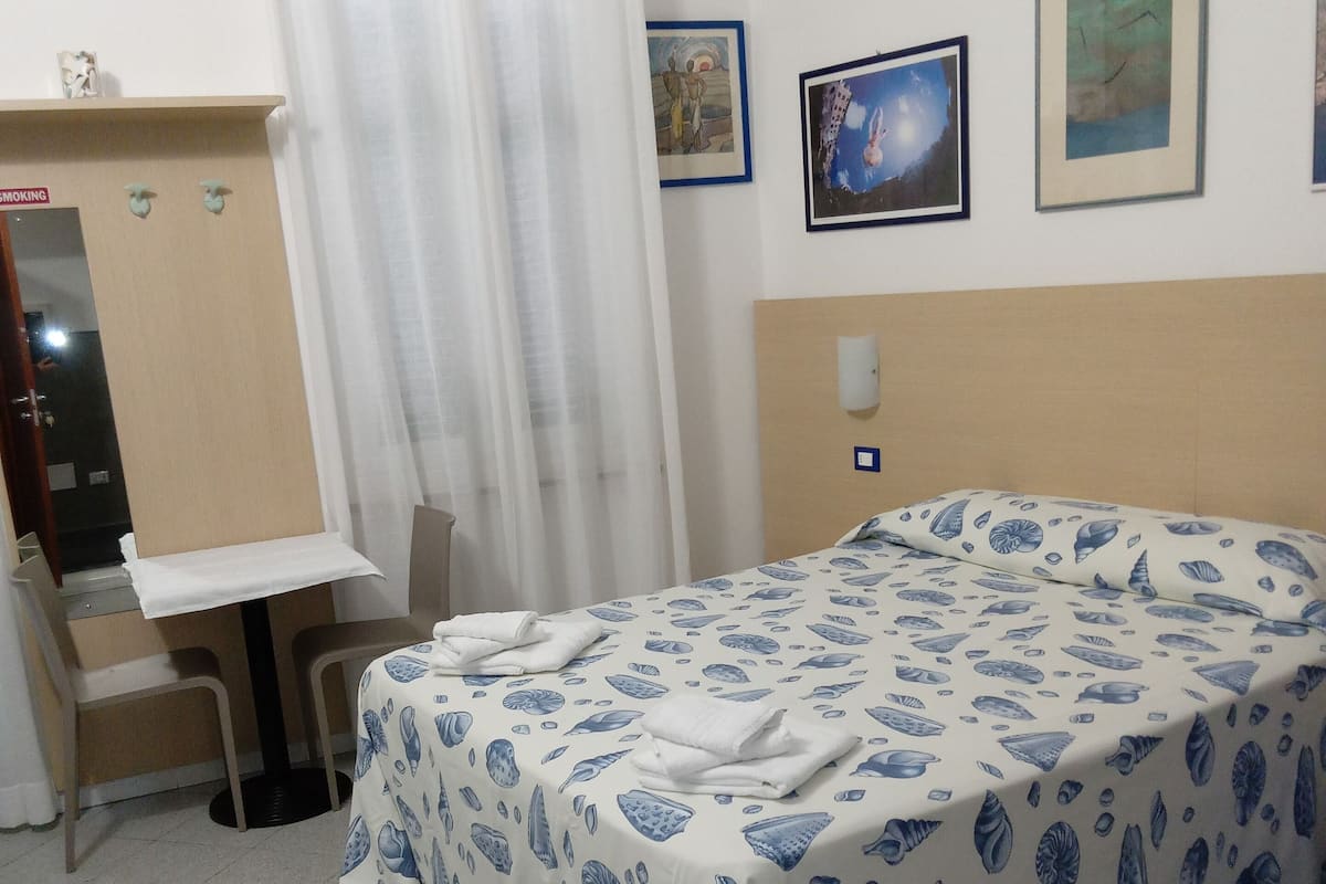 A hotel room with a bed, a desk, a chair, a mirror, and a window with curtains.