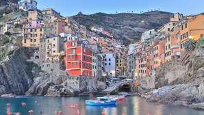 A coastal town with colorful buildings, a rocky shoreline, and boats in the water. - Il BoMa Affittacamere (Riomaggiore)