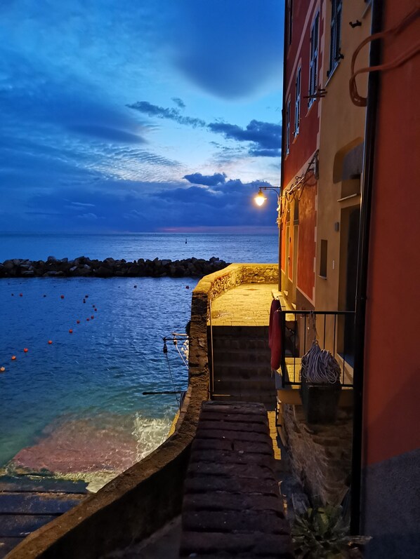 A narrow stone pathway leading to a building with a view of the sea.