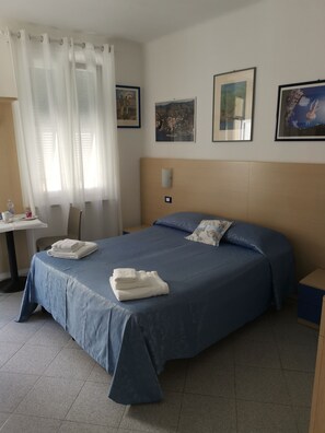 A hotel room with a bed, a desk, a chair, and a window with curtains.