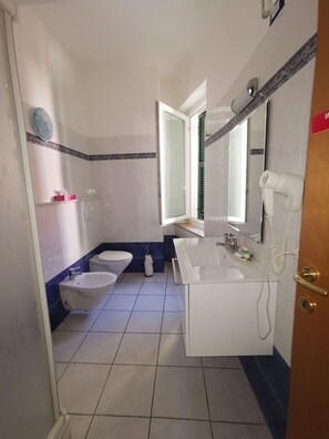 A bathroom with two sinks, a toilet, a mirror, and a hairdryer on the wall.