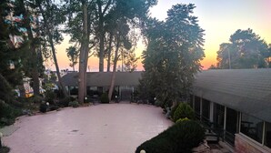 A courtyard with a tiled floor, surrounded by trees and a building with large windows. - Alhambra Palace Hotel Suites (Ramallah)