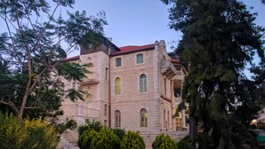 A historic building with a stone facade, multiple windows, and a red roof. - Alhambra Palace Hotel Suites (Ramallah)