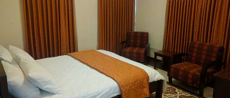 Quarto de hotel com cama, duas cadeiras, uma mesinha e ladrilhos no chão com padrão.
