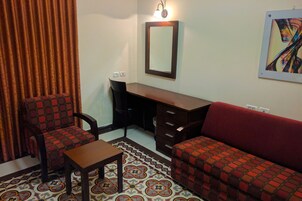 A room with a desk, two chairs, a sofa, a patterned rug, and a wall-mounted mirror.