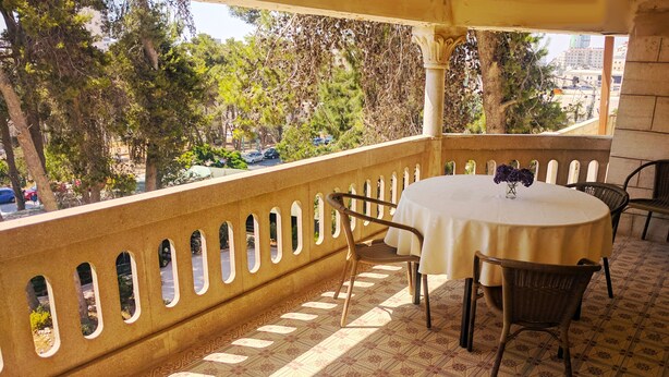 A balcony with a patterned floor, a round table with chairs, and a view of trees and buildings. - Alhambra Palace Hotel Suites (Ramallah)