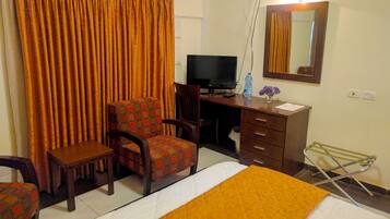 Ein Hotelzimmer mit Bett, Schreibtisch mit Computer, Stuhl, Spiegel und einem Fenster mit Vorhängen.