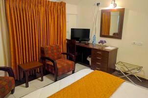 Habitación de hotel con cama, escritorio, computadora, silla, espejo y ventana con cortinas.