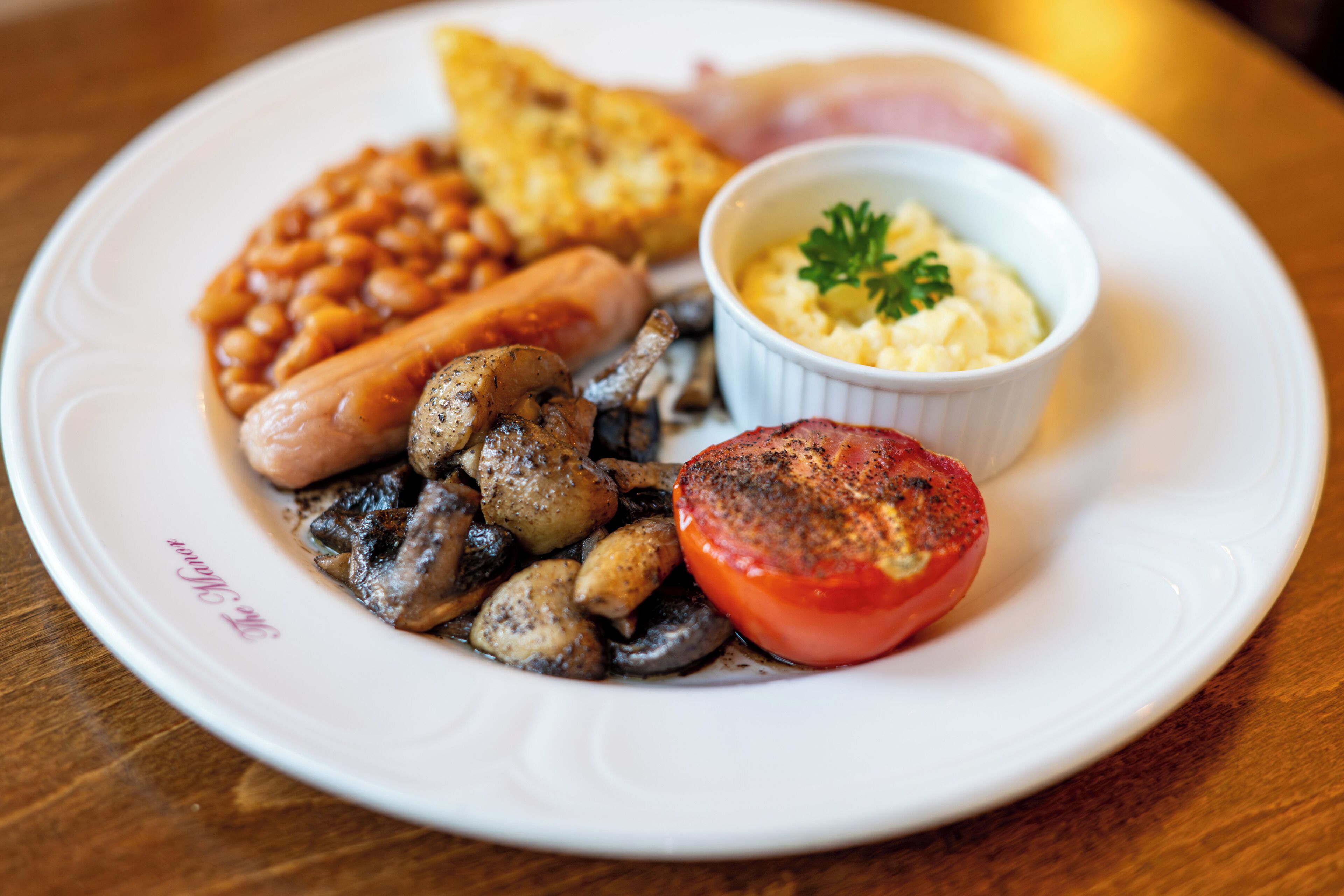 Ein Teller mit Bohnen, Würstchen, Pilzen, einer gegrillten Tomate, Rührei und Toast.