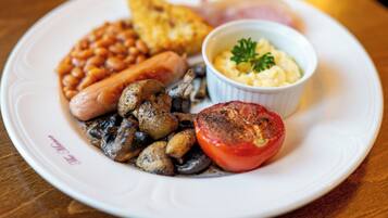 Ein Teller mit Bohnen, Würstchen, Pilzen, einer gegrillten Tomate, Rührei und Toast.