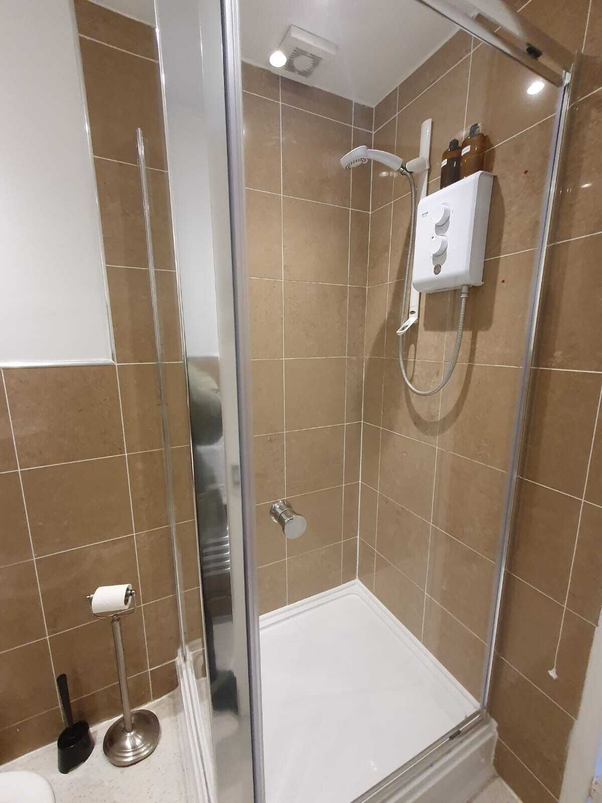 A modern bathroom with a glass-enclosed shower, beige tiles, and a white toilet paper holder.