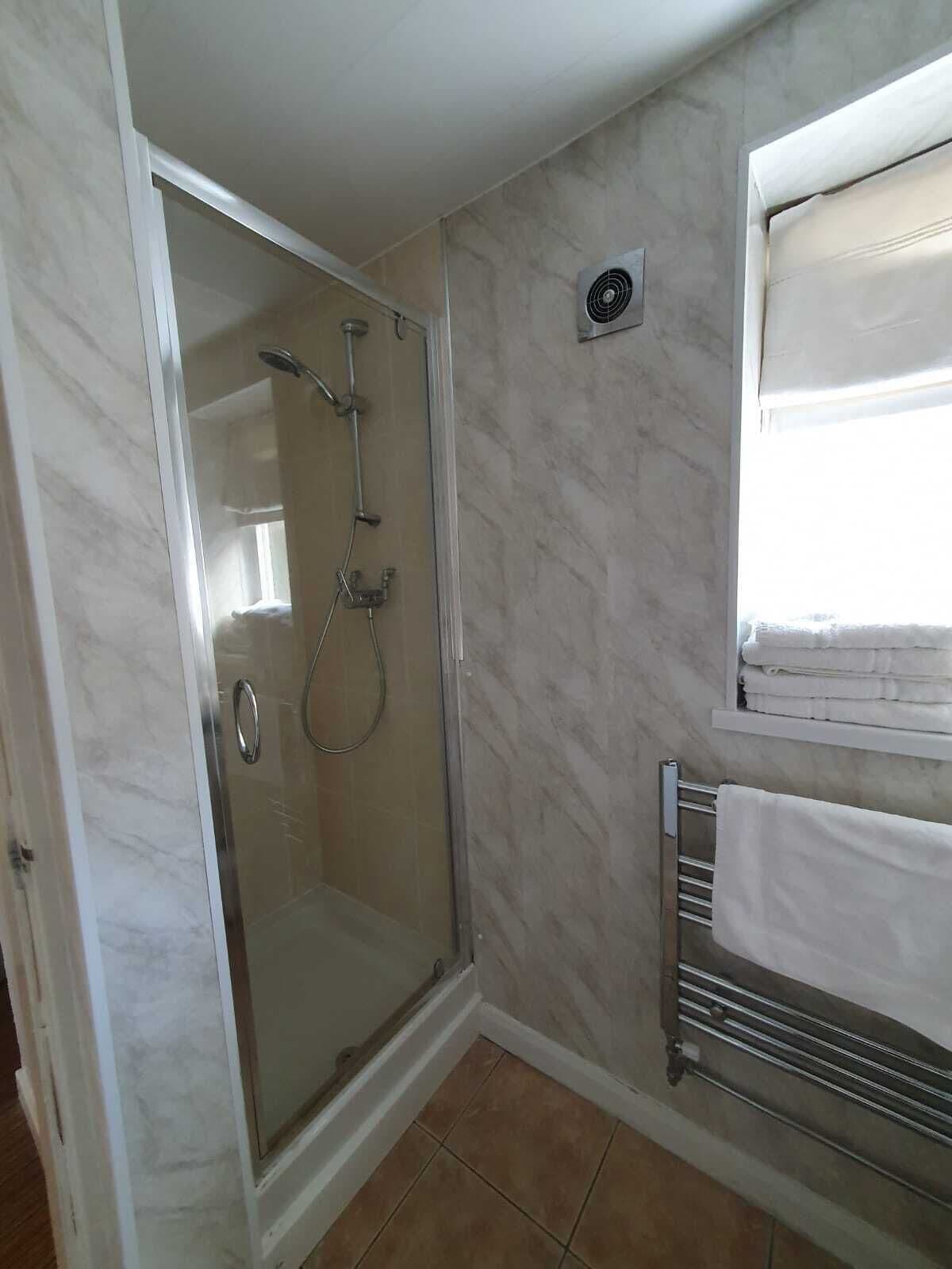 A bathroom with a glass-enclosed shower, a towel rack, and a window with curtains.