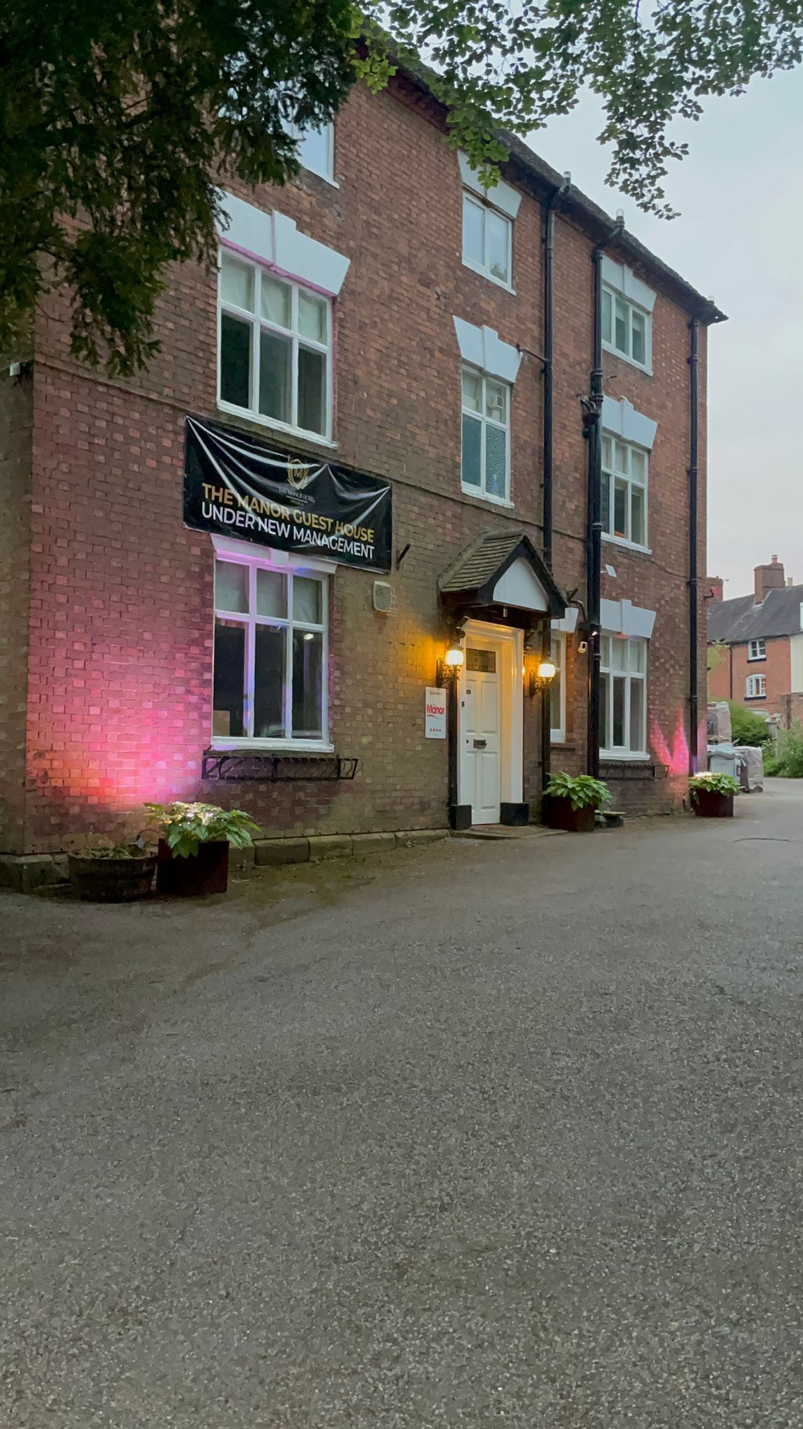 A brick building with a sign reading "The Manor Guest House Under New Management."