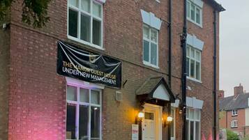 A brick building with a sign reading "The Manor Guest House Under New Management."