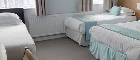 A hotel room with two beds, a radiator, and a window with curtains.