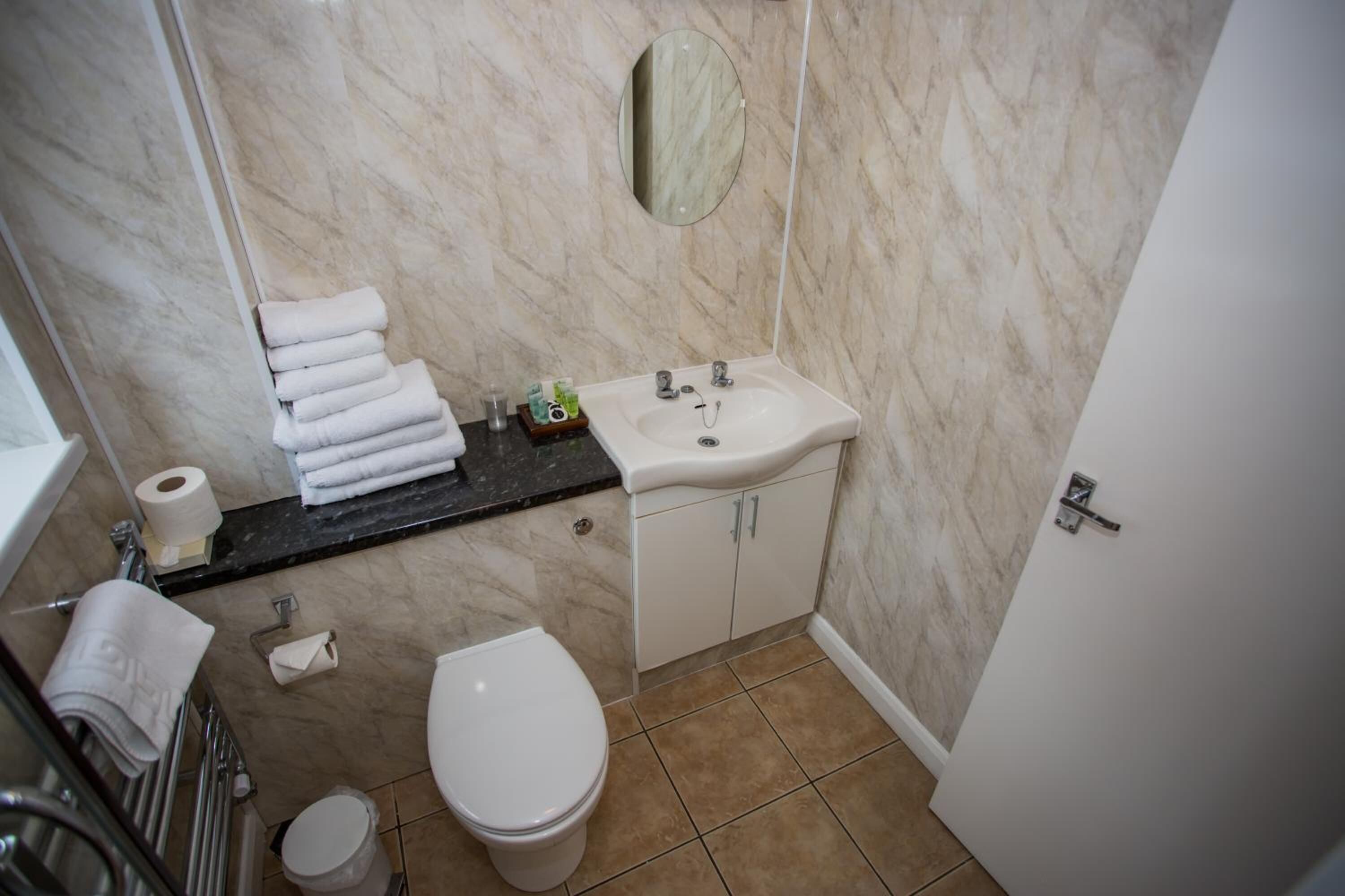 A bathroom with a marble wall, a sink, a toilet, and a towel rack with folded towels.