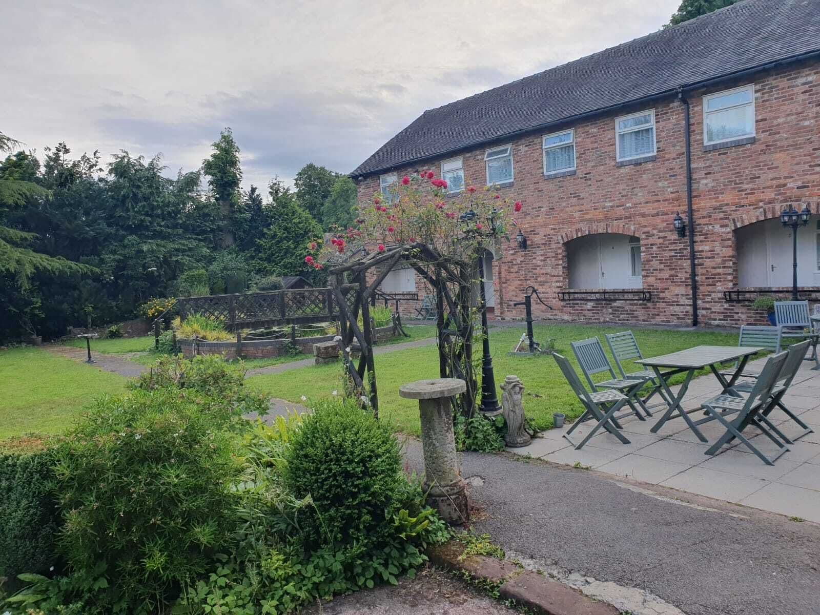 Een bakstenen gebouw met een tuin, een terras, zitplaatsen buiten en een pergola begroeid met klimplanten.