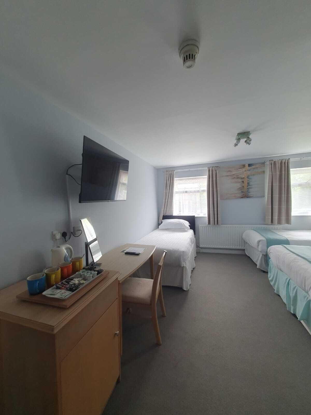 A hotel room with a desk, two beds, a TV, and a window with curtains.