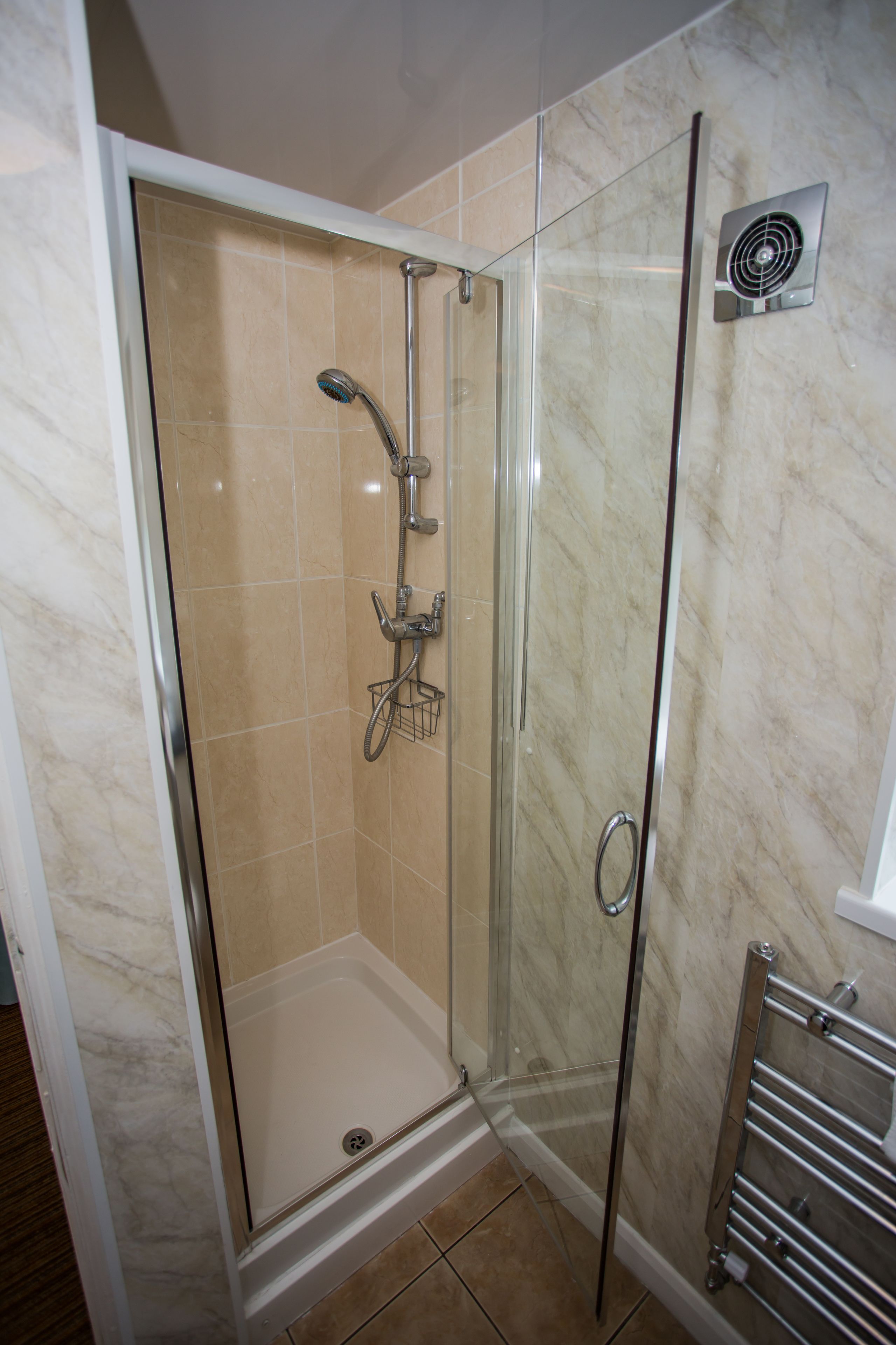 A glass-enclosed shower stall with a handheld showerhead, a handheld shower head, and a wall-mounted fan.