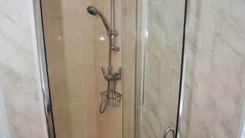 A glass-enclosed shower stall with a handheld showerhead, a handheld shower head, and a wall-mounted fan.
