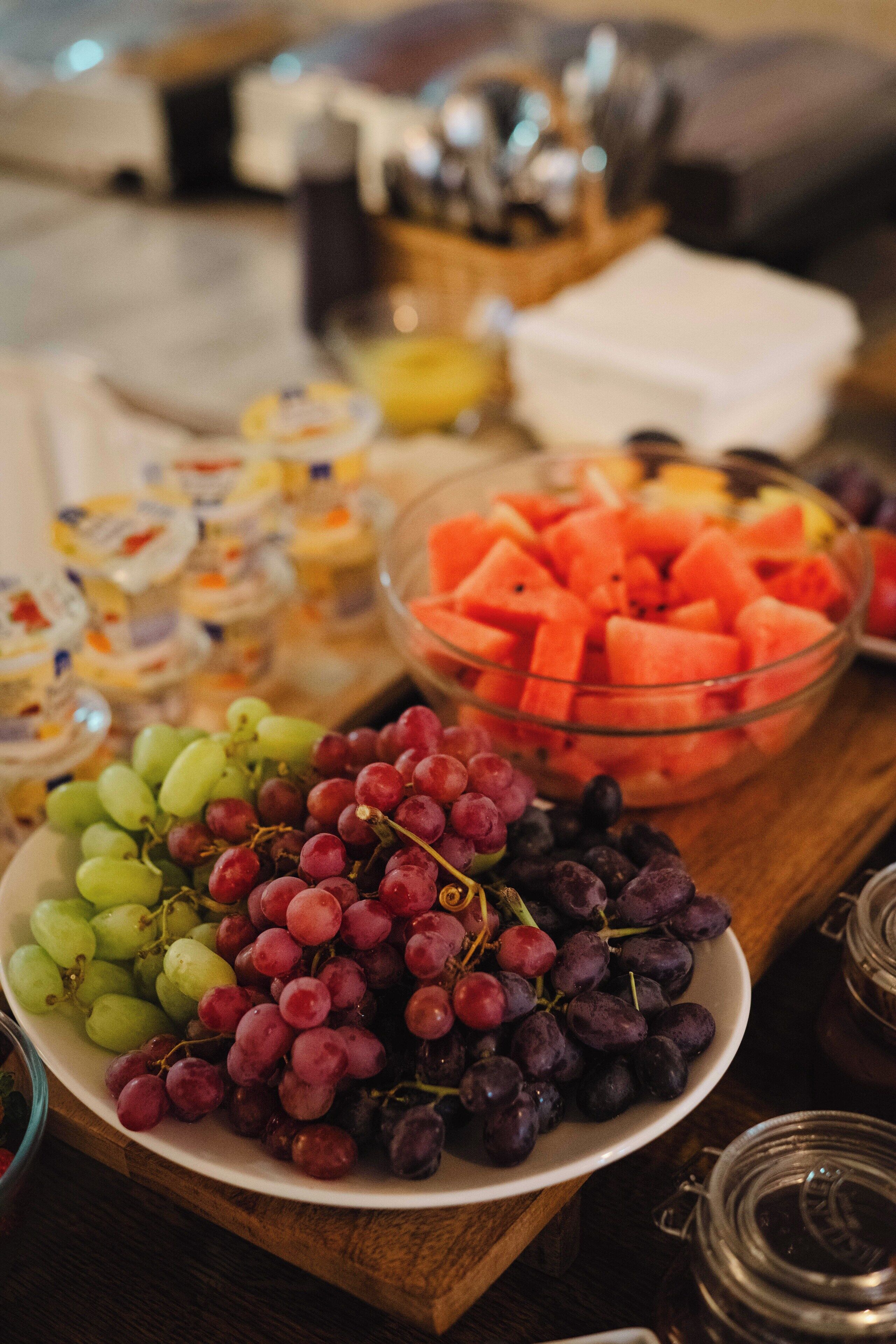 A table with various food items including bowls of grapes, watermelon, and other fruits.