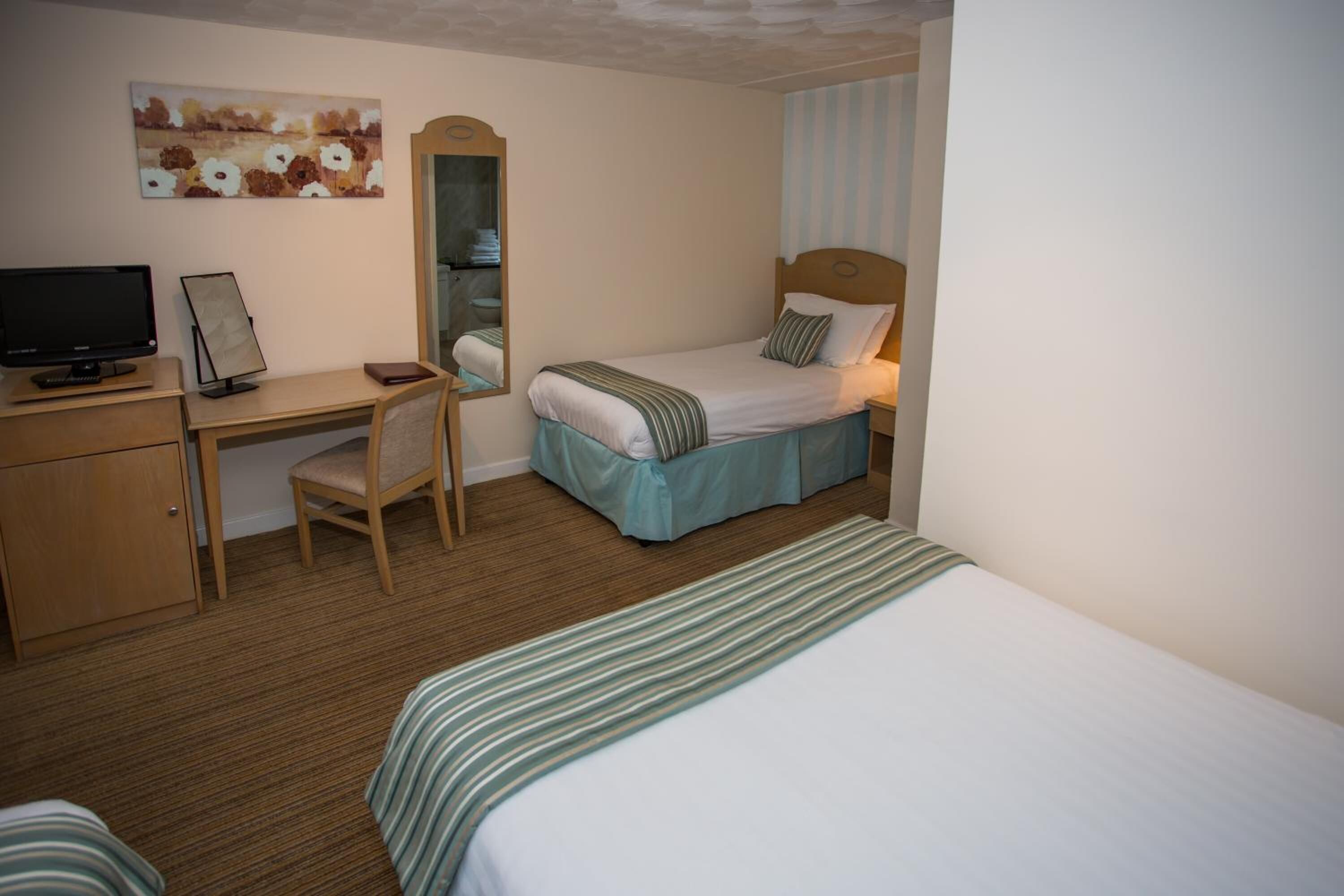 A hotel room with a bed, a desk with a computer, a chair, a mirror, and a television.