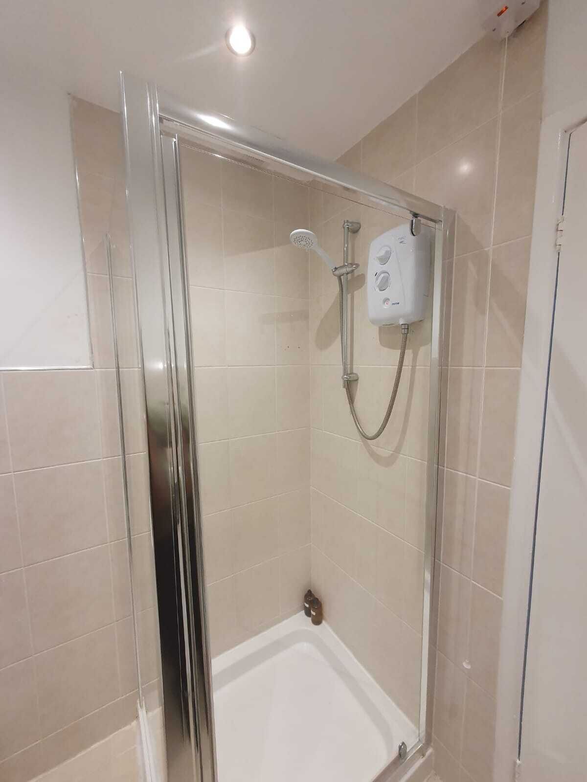 A glass-enclosed shower stall with a handheld showerhead and a wall-mounted control panel.