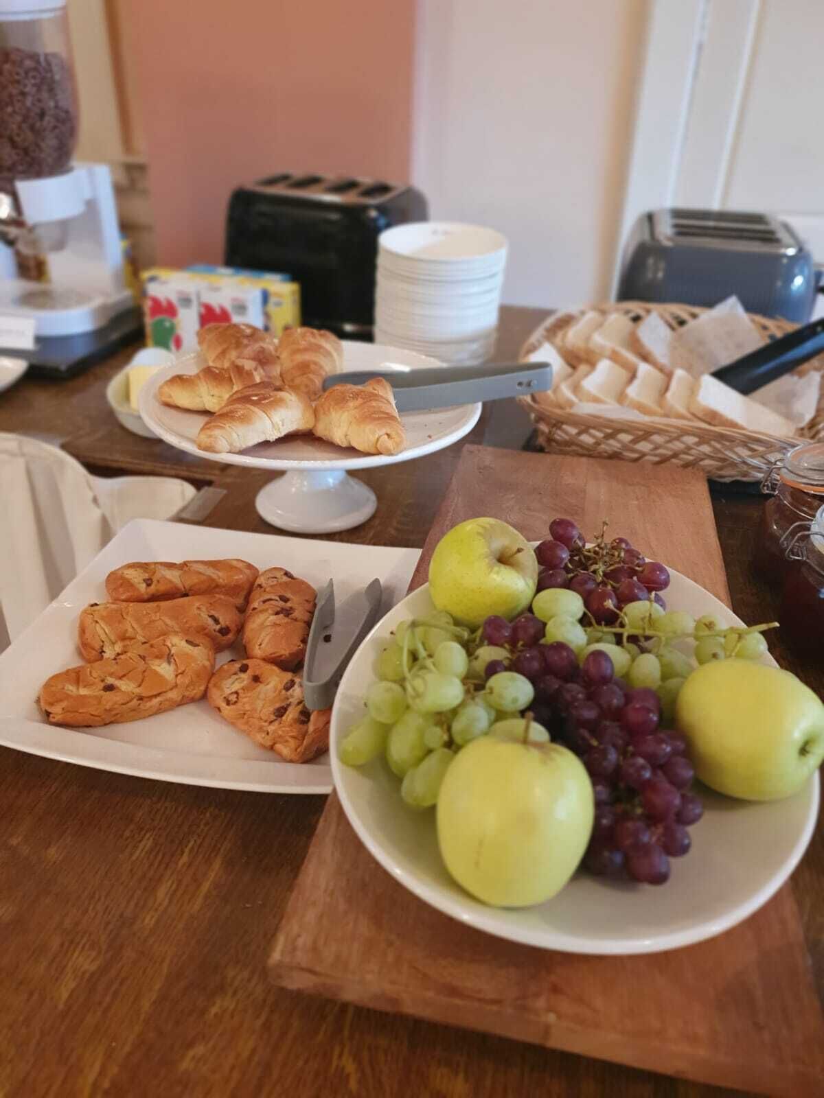 A breakfast table with croissants, a plate of fruit, and a basket of bread.
