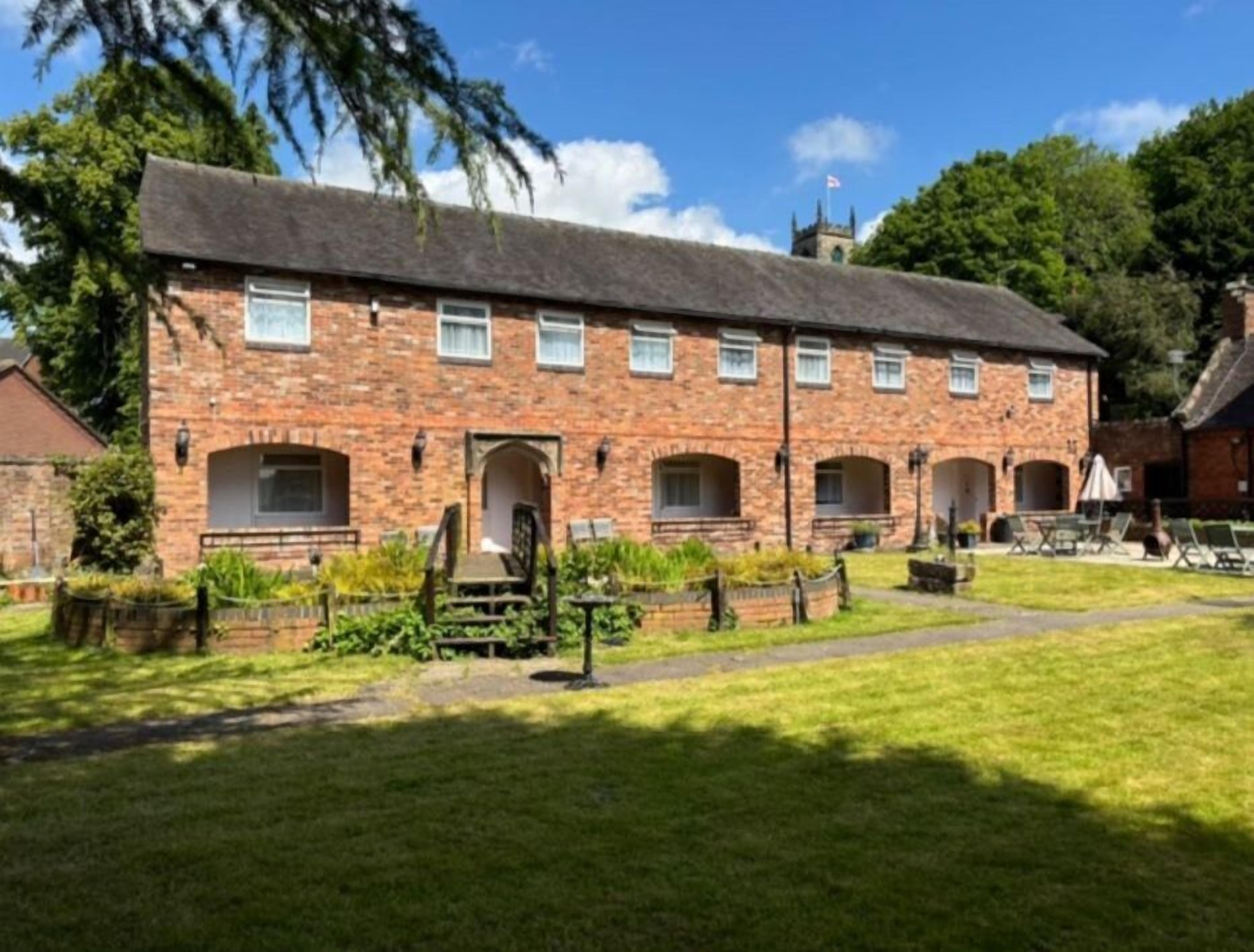 A brick building with multiple rooms, a garden, and a small tower in the background.
