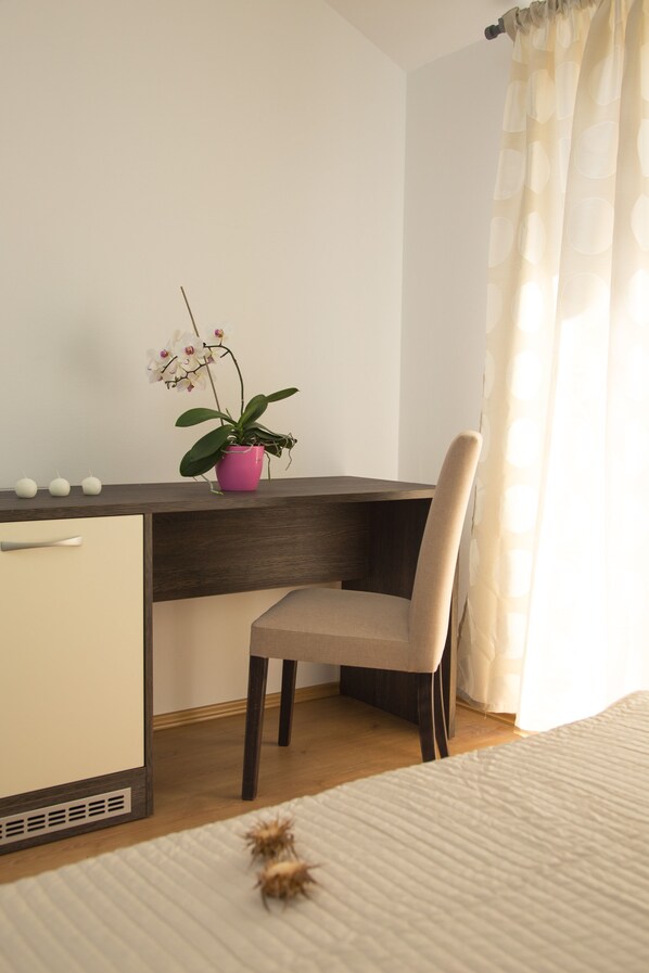 Un dormitorio con cama, un escritorio con silla, una pequeña planta en maceta y una ventana con cortinas.