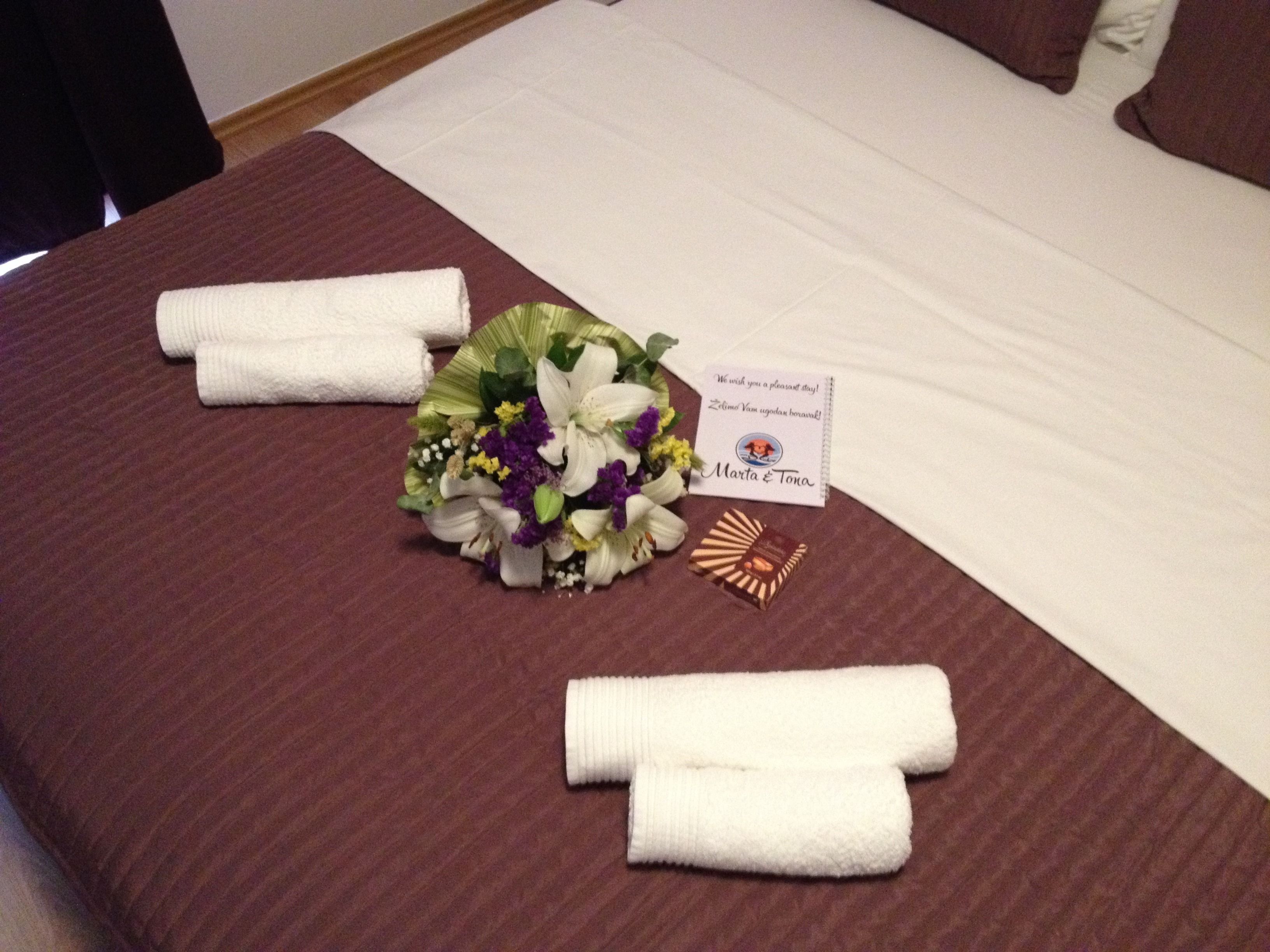 A neatly made bed with white linens, a bouquet of flowers, and a small card on the bed.