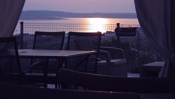 Una terraza con mesa y sillas, con vista a la puesta de sol sobre el agua.