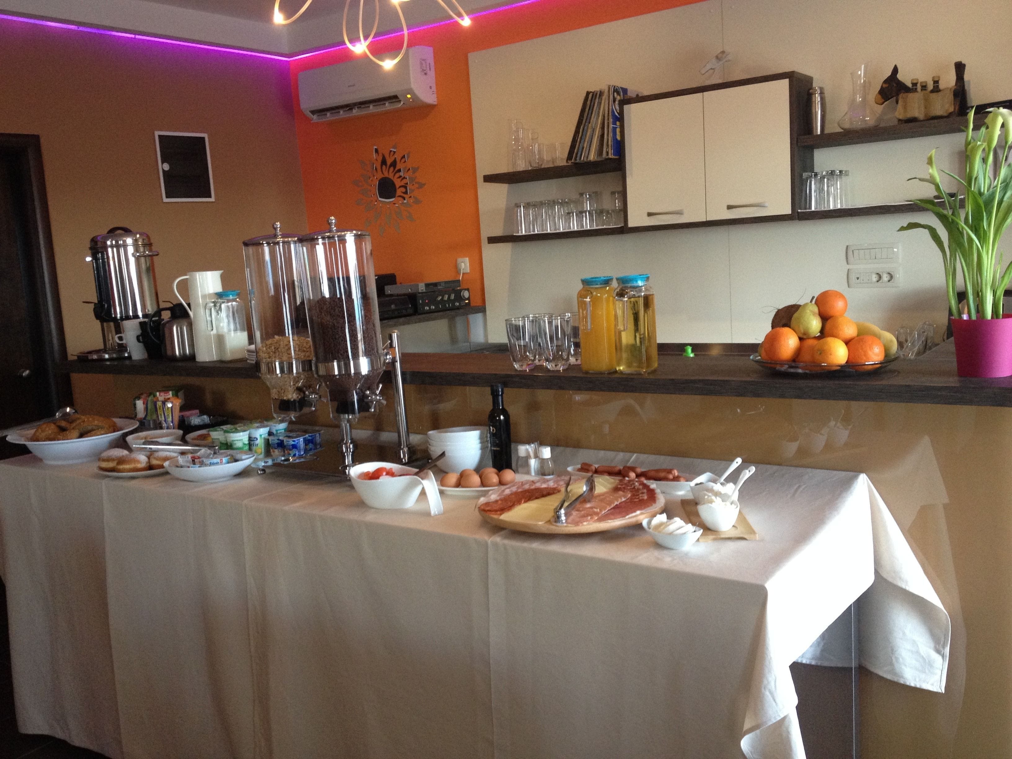 A breakfast buffet with various food items and beverages, a coffee machine, and a potted plant on the counter.
