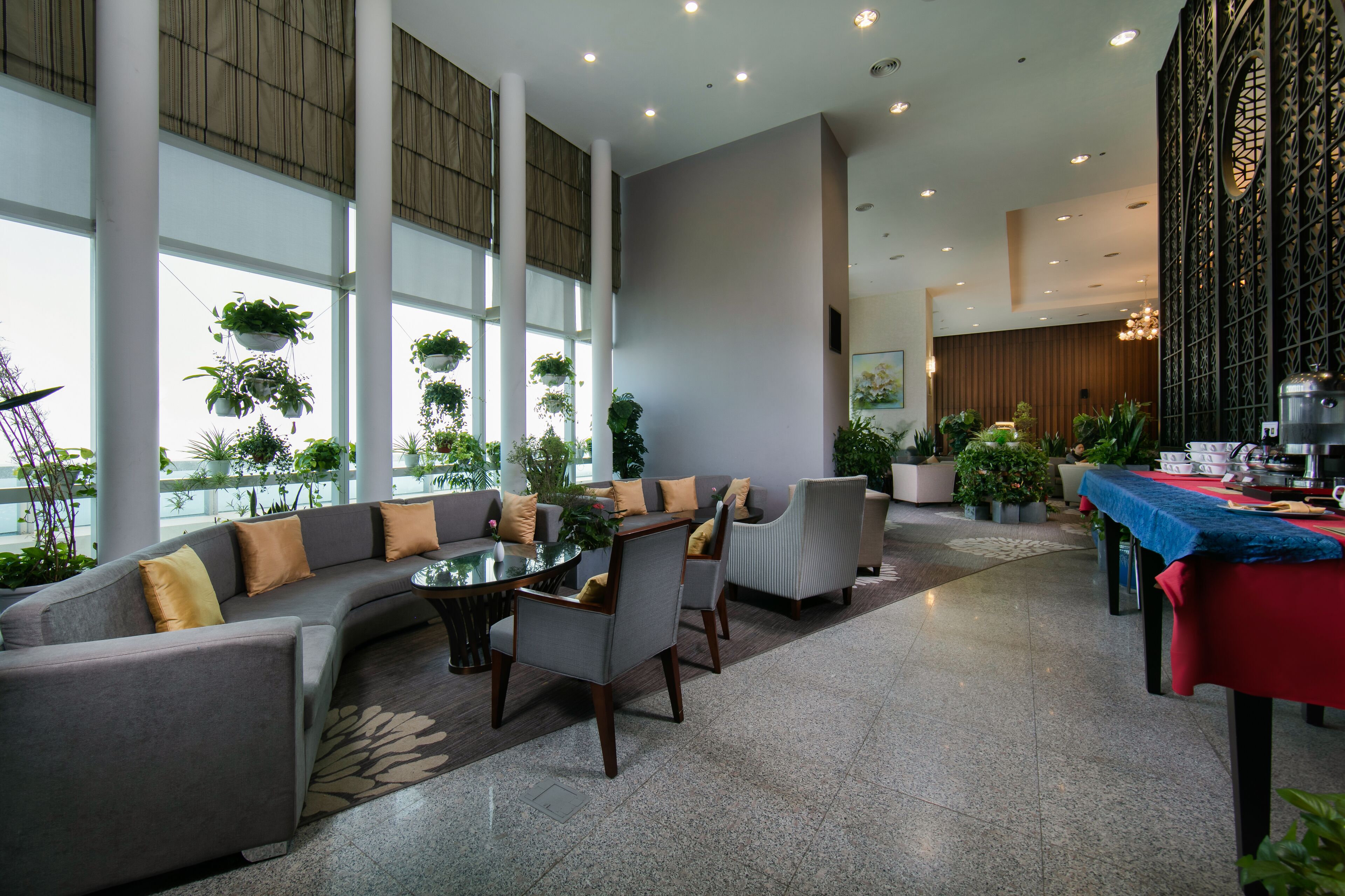 A modern hotel lobby with a seating area, a dining table, and a kitchen area.