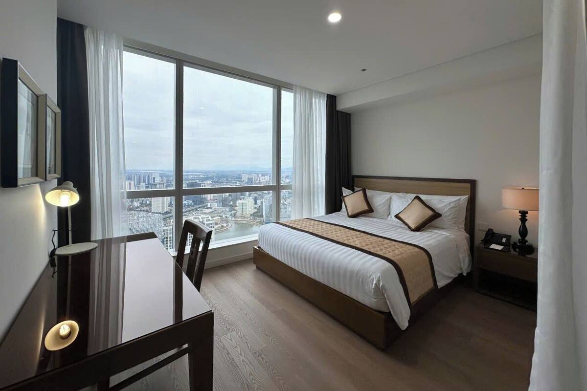 Een hotelkamer met een groot bed, een bureau en uitzicht op de stad door grote ramen.