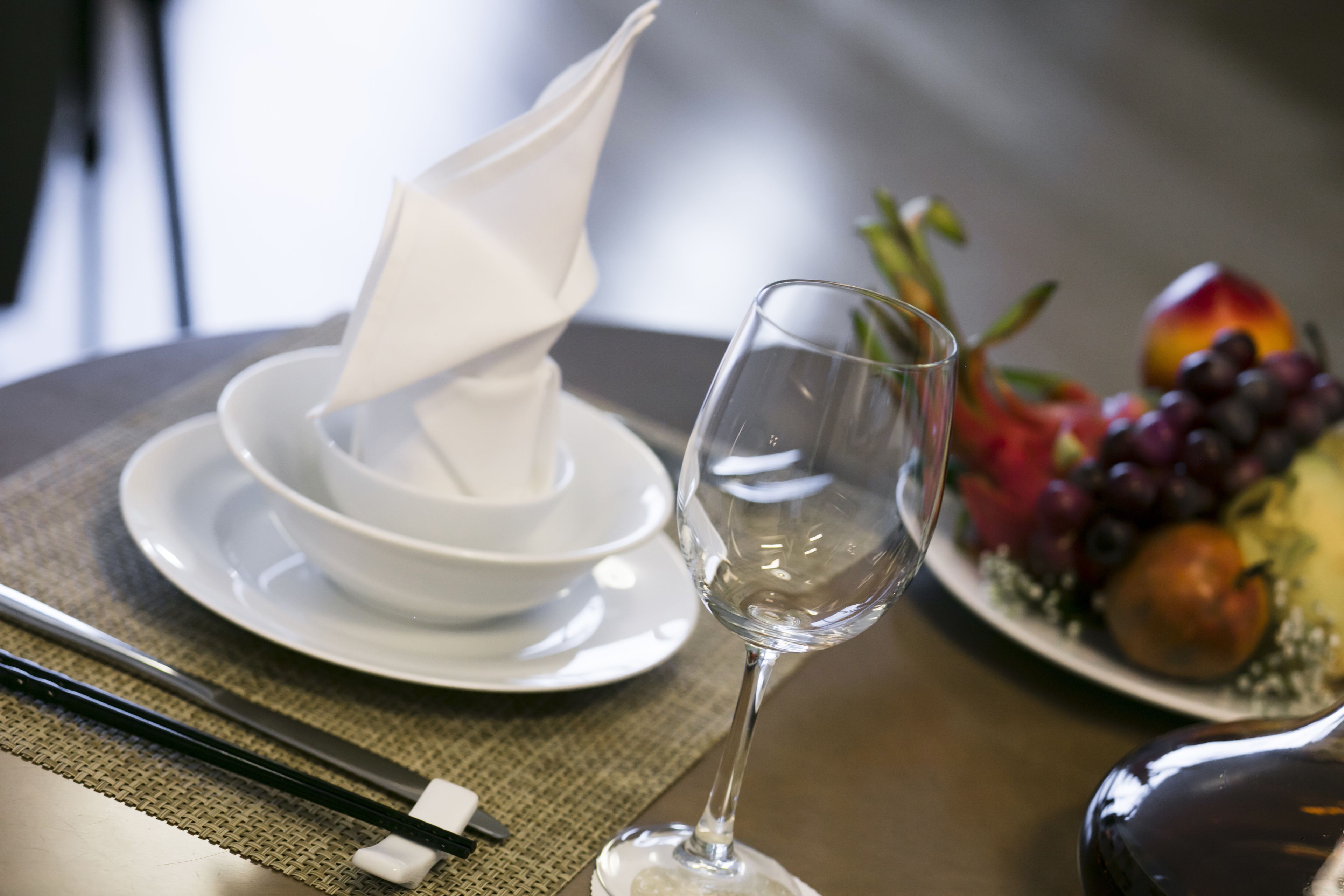 A dining table with a white napkin, a wine glass, chopsticks, and a plate of fruit.