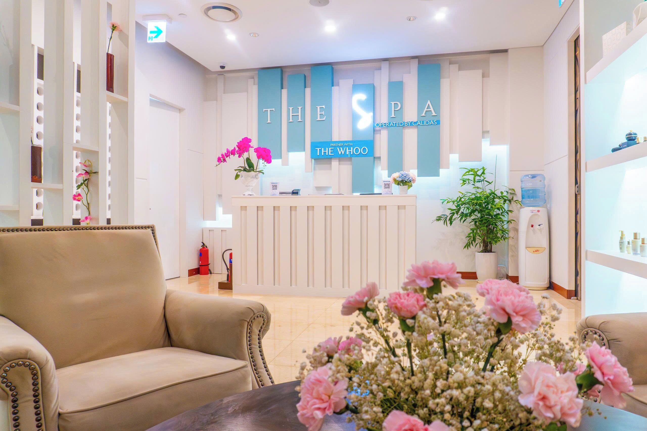 A reception area with a reception desk, beige sofas, a vase of pink flowers, and a sign that reads 'THE SPA'.