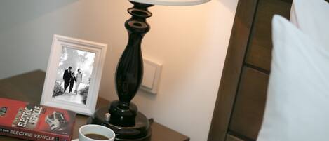 Camera d'albergo ordinata con un comodino che include una lampada, una cornice con una foto, un libro e una tazza di caffè.