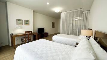 A hotel room with two beds, a desk with a chair, a TV, and a lamp.