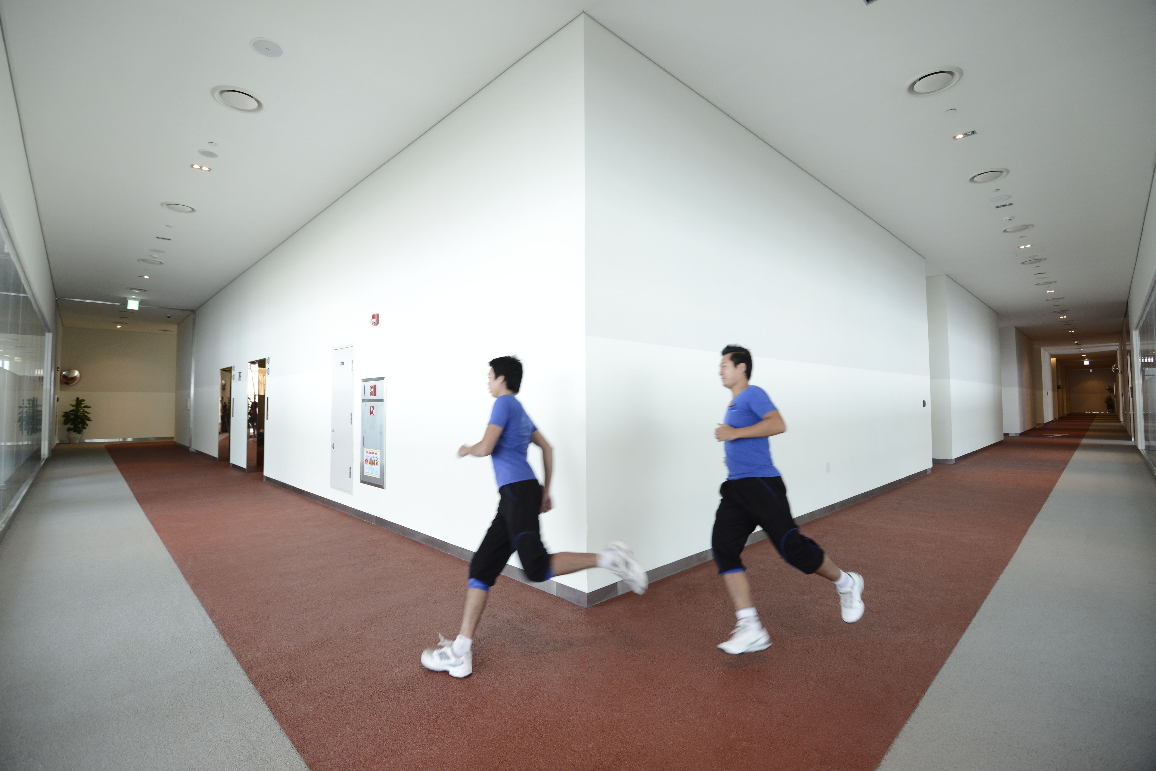 A corridor with a red carpet, white walls, and a ceiling with recessed lighting.