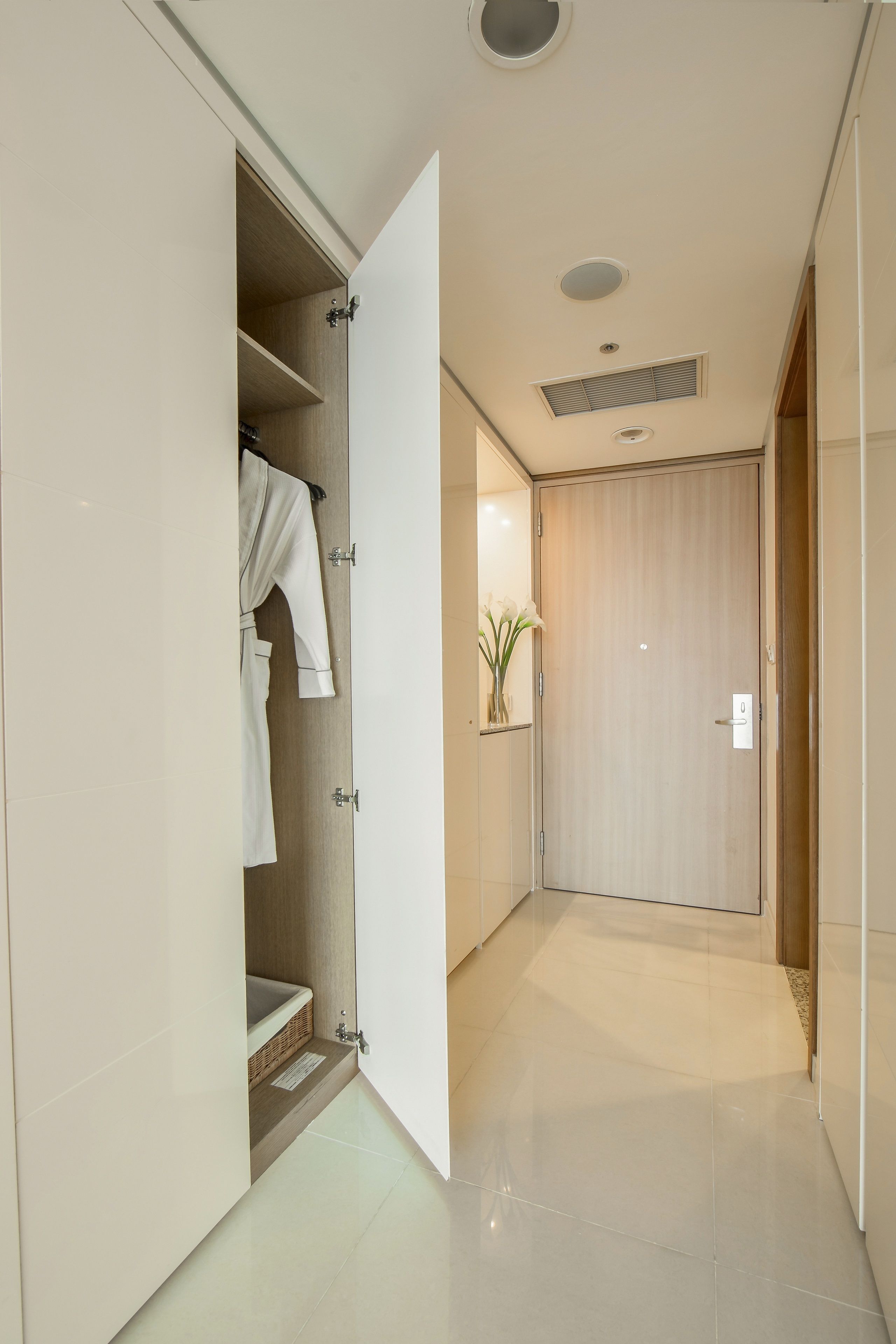 A hallway with a wooden door, a white robe hanging, and a small plant on a shelf.