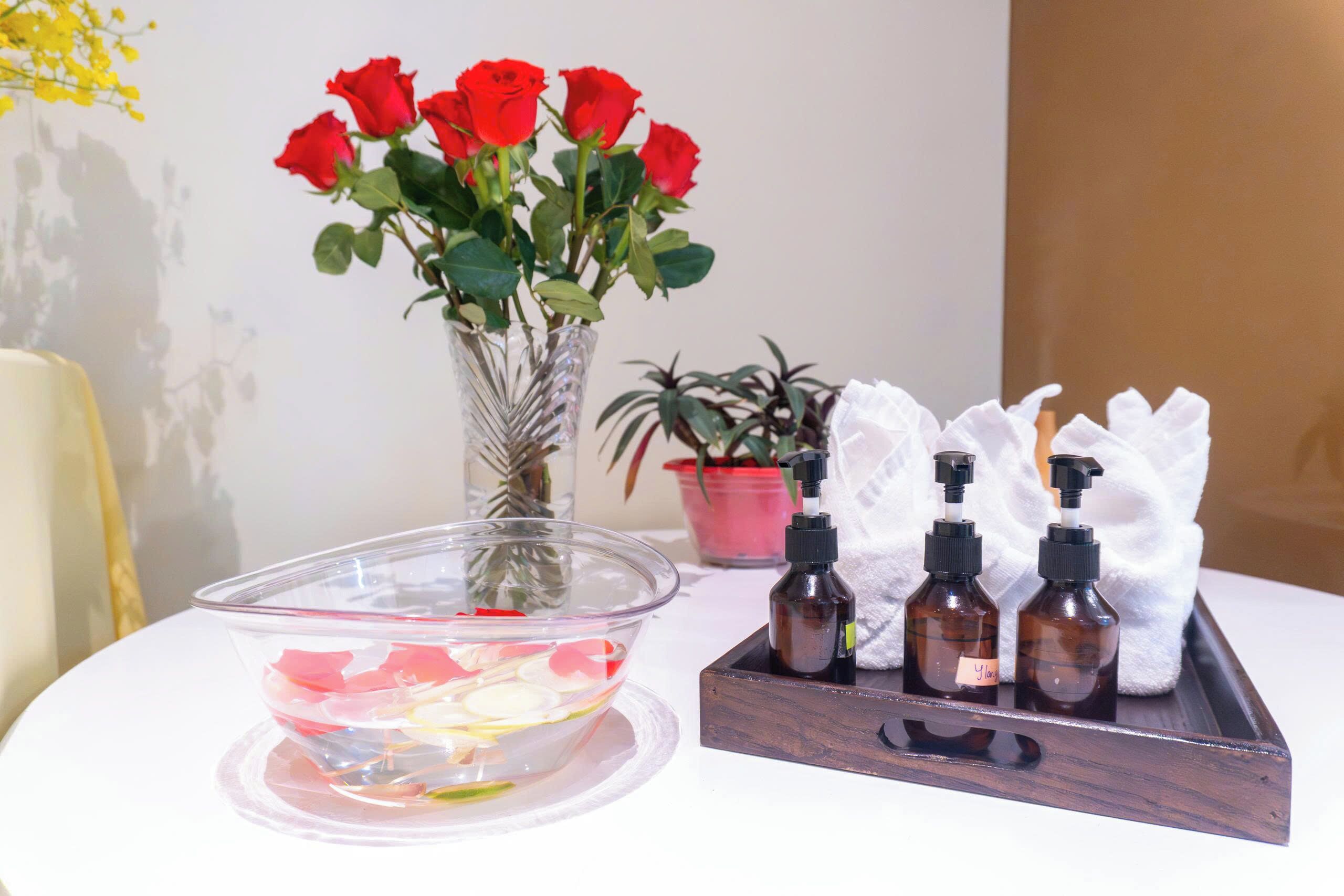A clear glass bowl with flower petals, a vase with red roses, and two small bottles with pumps on a tray.