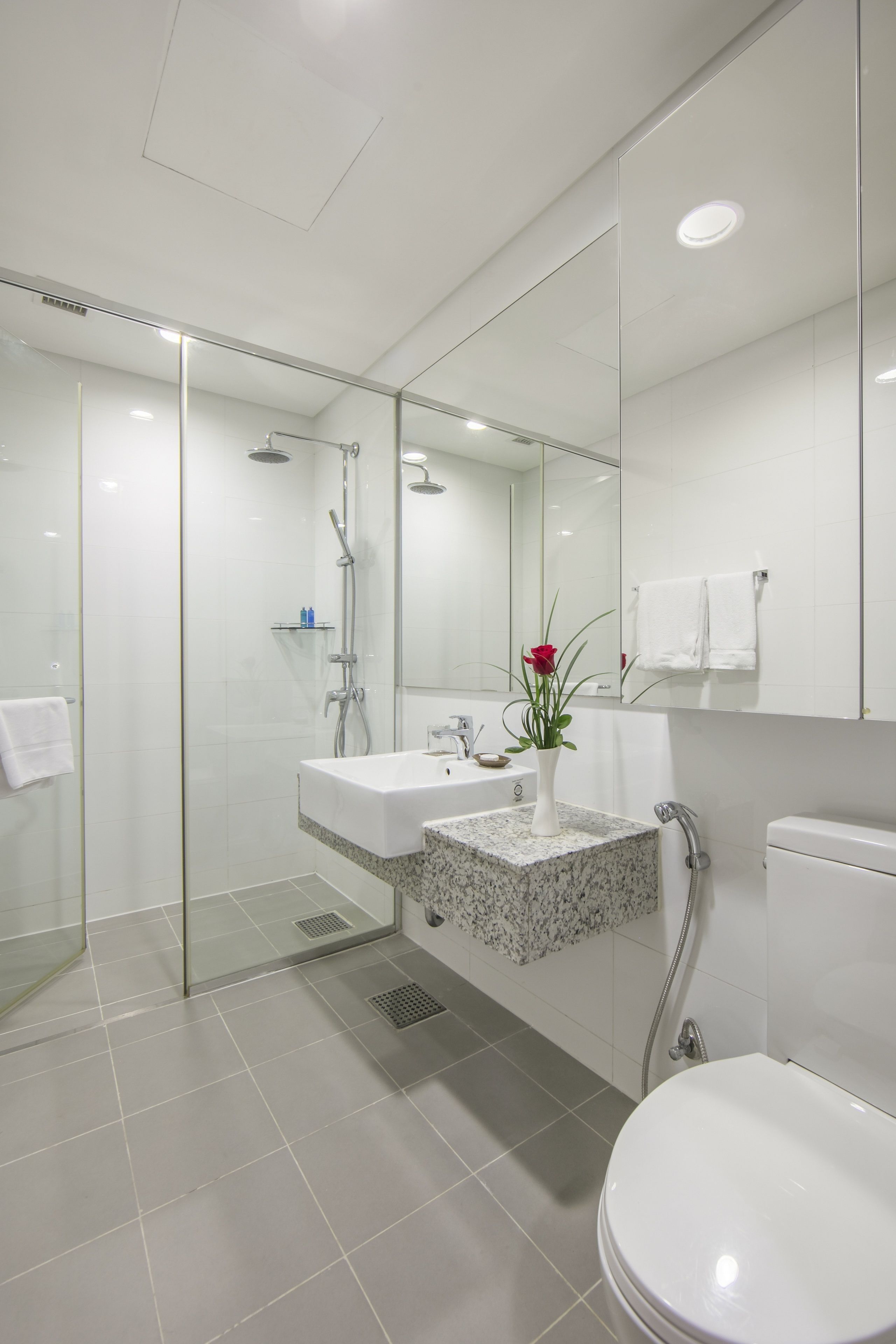 A modern bathroom with a glass-enclosed shower, a white sink with a marble countertop, and a toilet.