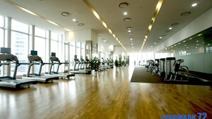 Ein großzügiger Fitnessraum mit mehreren Laufbändern und Trainingsgeräten, großen Fenstern und einem Holzboden.